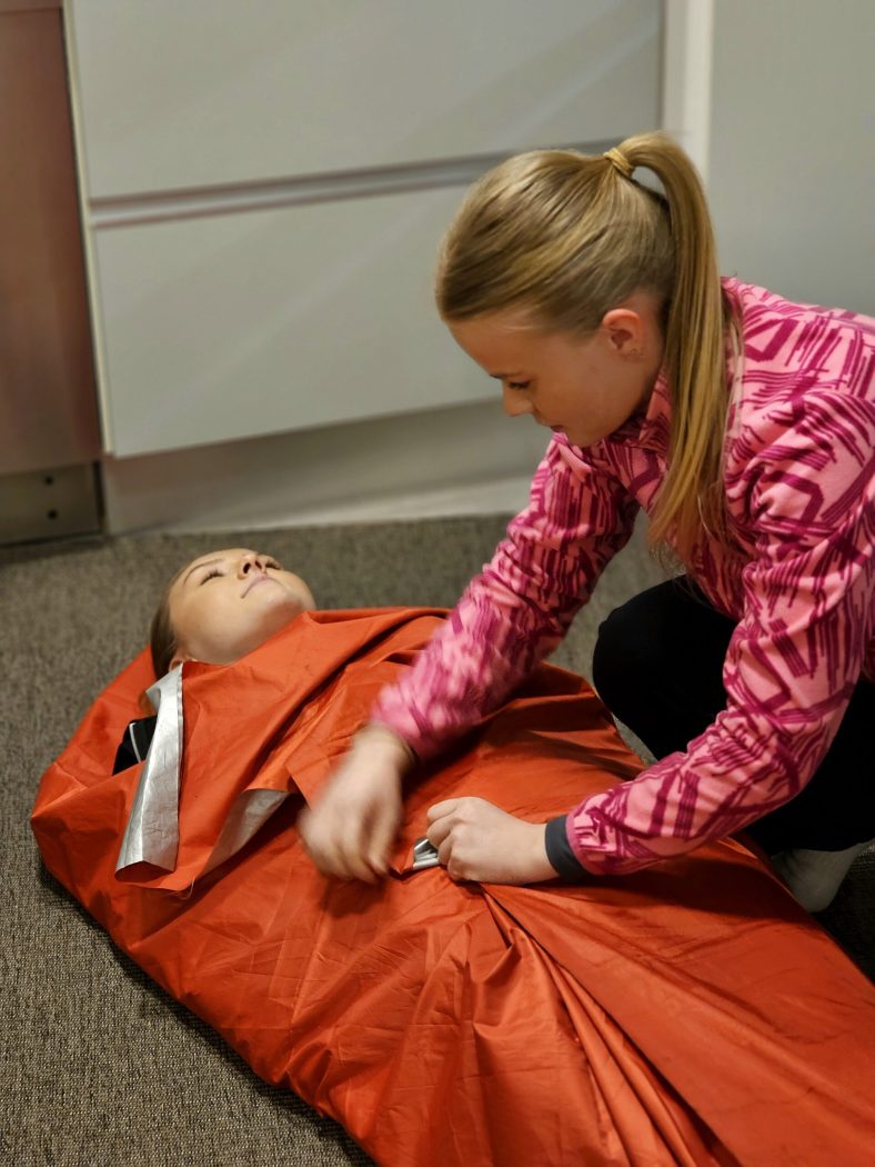 Ensiapukoulutuksessa nainen laittaa toisen naisen suojapeitteeseen